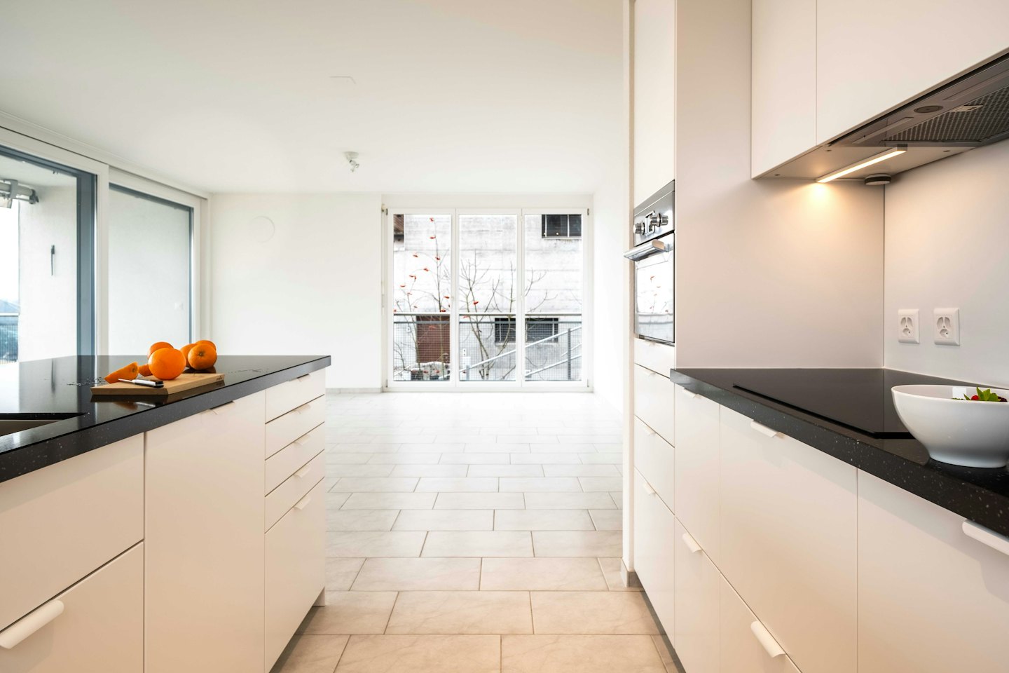 Modern kitchen with white cabinets, dark countertops, and oranges on a cutting board.