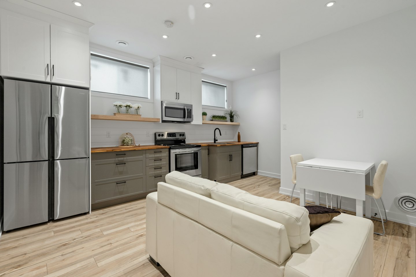 Modern open-concept kitchen with grey and white cabinets and light wood counters.